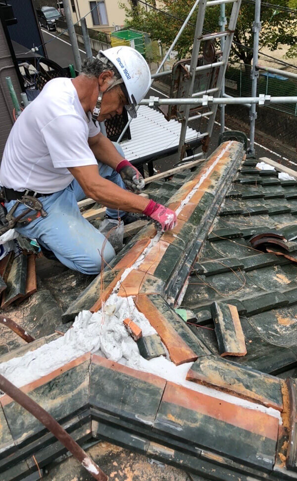 中部OKペイントの屋根防止工事施工例。熟練な職人が手稲に瓦屋根の溝を埋めている。