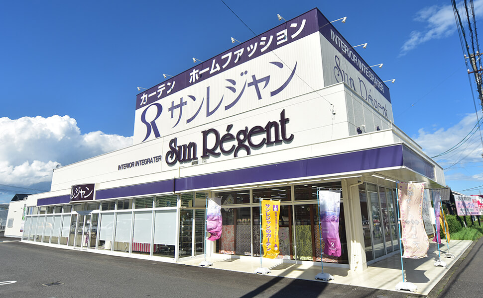 愛知県稲沢市に位置するカーテン専門店サンレジャン。一宮店の店舗外観。白のベースに紫色でサンレジャンの文字とラインが走る。